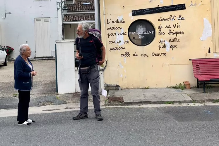 Hervé Pauchon dans une rue d'un village discutant avec une habitante